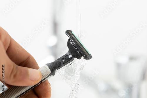 man's hand holding razor under running water in bathroom 