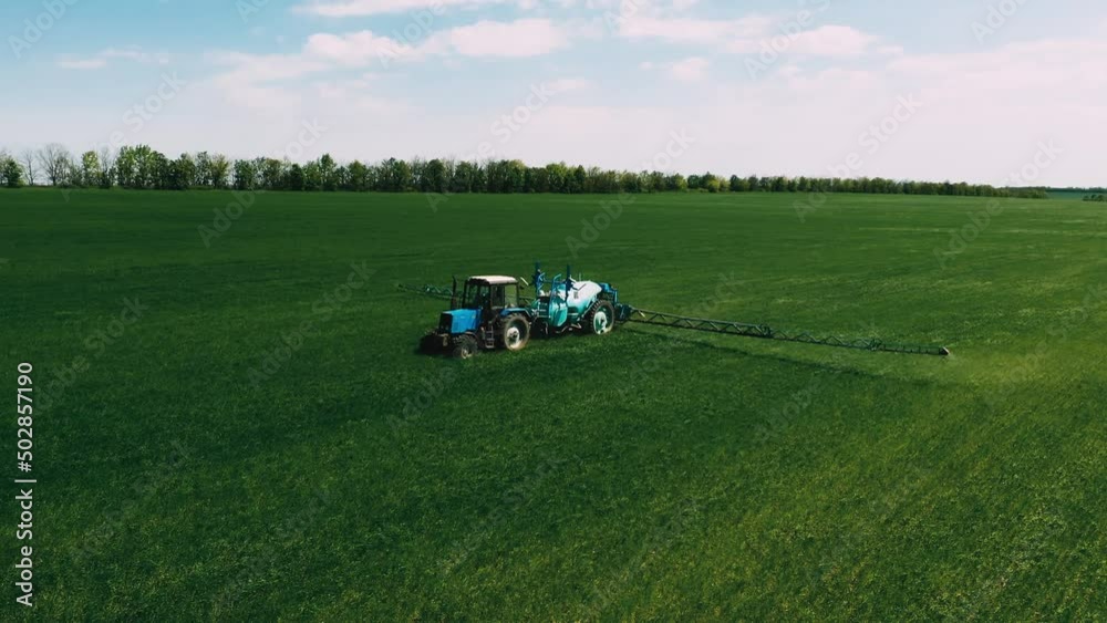 Aerial view of a tractor operating in green fields. The tractor sprays water or fertilizer on wheat, cereals, rye or corn flakes. The process is part of agriculture and growing food for mass consumpti Aerial view of a tractor operating in green fields. The tractor sprays water or fertilizer on wheat, cereals, rye or corn flakes. The process is part of agriculture and growing food for mass consumpti