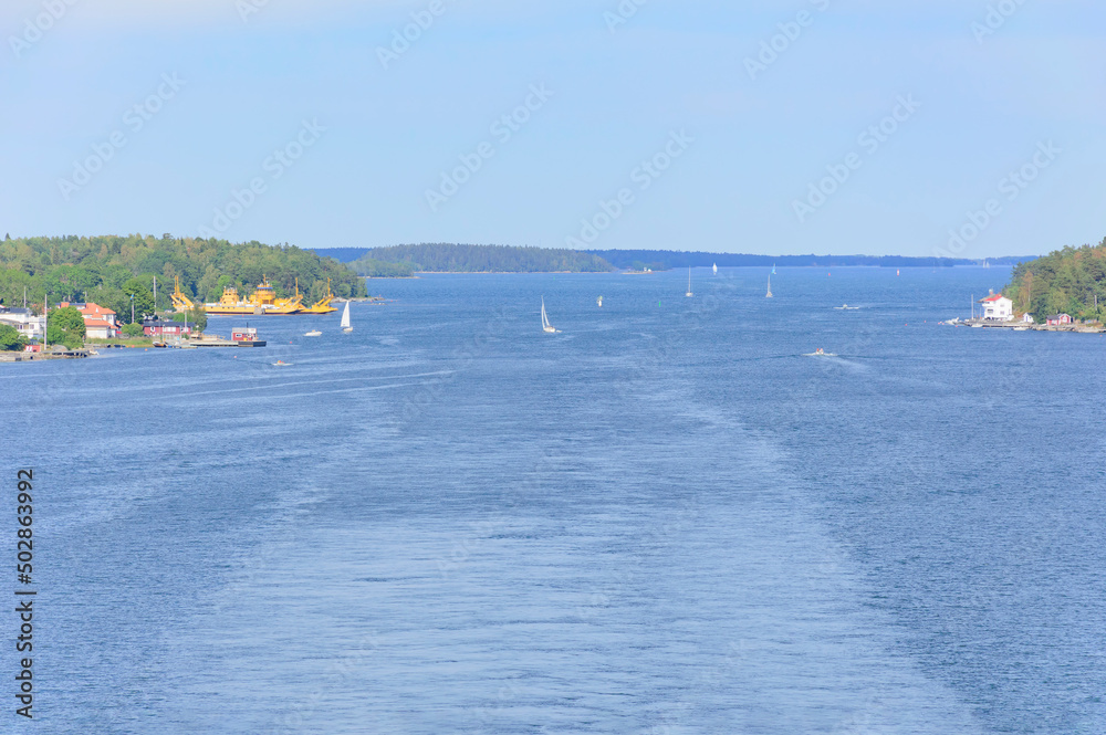 Obraz premium view of the Stockholm fiord from a ferry deck. Blue sea water, green forest on the shores, many small sailboats
