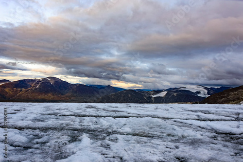 Evening on the glacier on the trail from Galdhopiggen summit in Norway. White and grey ice, dark mountains, sunset sky with clouds