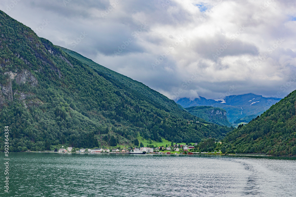 View of Geirangerfjord in Norway. Green and grey sea water, cloudy sky, green and blue mounain slopes