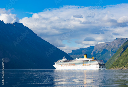 Cruise ship in the sea. Blue water of Geirangerfjord, dark blue and green Norwegian mountains, light blue sky with clouds