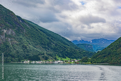 View of Geirangerfjord in Norway. Green and grey sea water, cloudy sky, green and blue mounain slopes