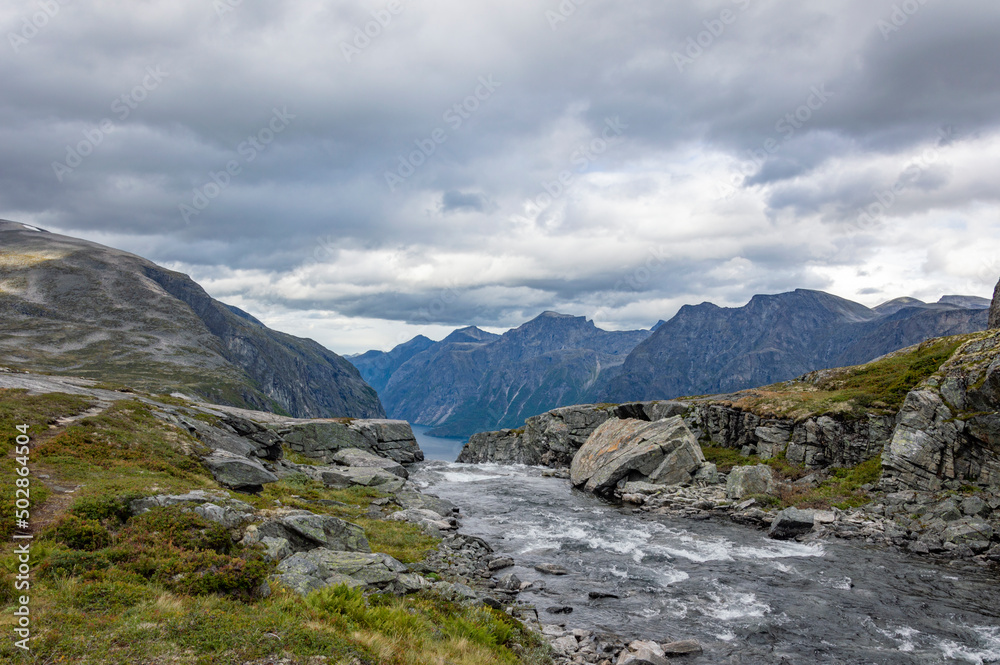 View of the landscape with the source of the Mardalsfossen waterfall in Norway. Grey sky with clouds, grey mossy rocks, white water of the mountain stream