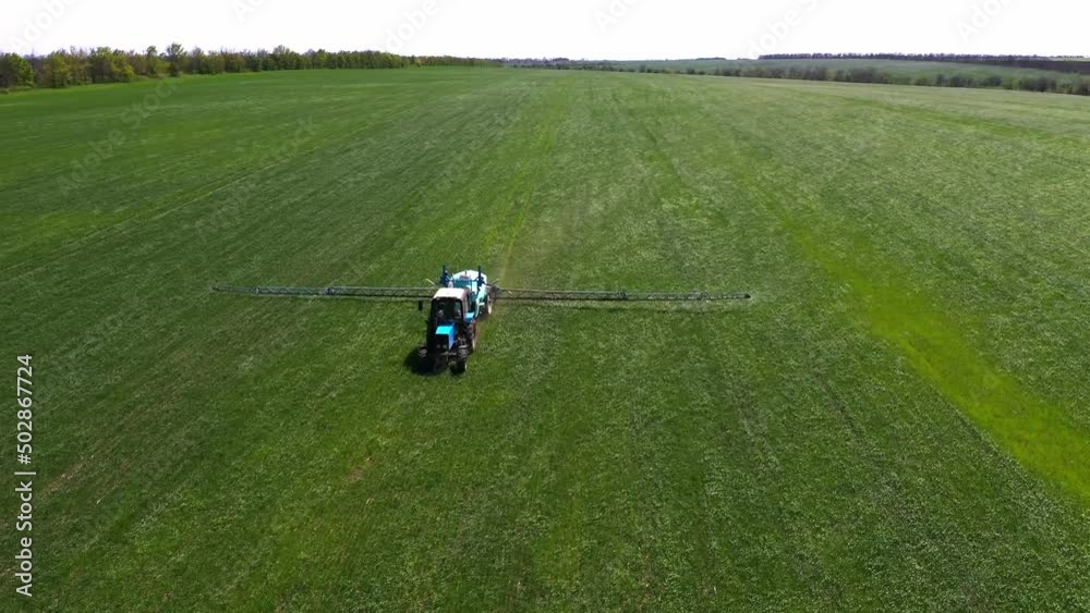 Spraying a green wheat field by tractor. The farming tractor spraying on field with sprayer, herbicides and pesticides. Industrial machine fertilizing a field. Chemicals used by agricultural tractor. Spraying a green wheat field by tractor. The farming tractor spraying on field with sprayer, herbicides and pesticides. Industrial machine fertilizing a field. Chemicals used by agricultural tractor.