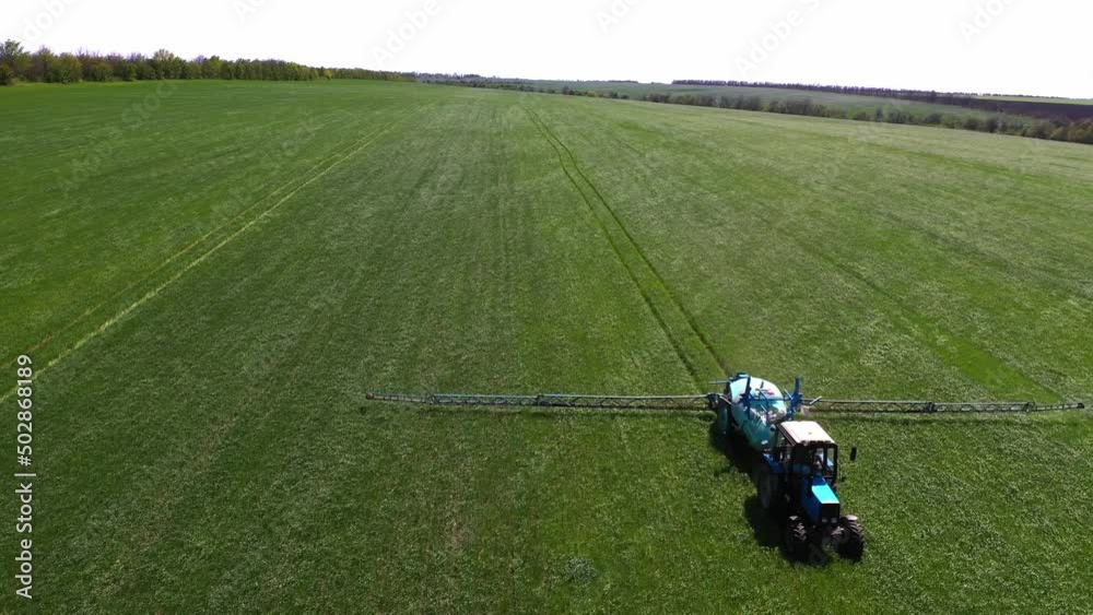 Spraying a green wheat field by tractor. The farming tractor spraying on field with sprayer, herbicides and pesticides. Industrial machine fertilizing a field. Chemicals used by agricultural tractor. Spraying a green wheat field by tractor. The farming tractor spraying on field with sprayer, herbicides and pesticides. Industrial machine fertilizing a field. Chemicals used by agricultural tractor.