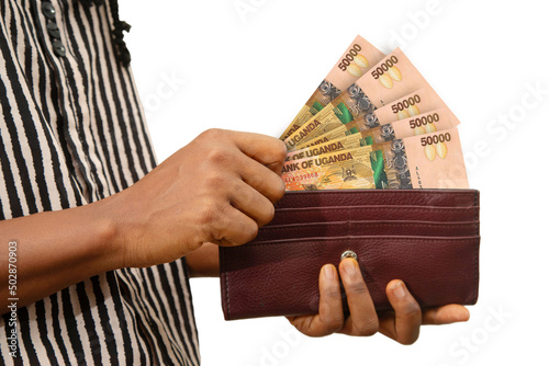 fair Female Hand Holding brown Purse With Ugandan shilling notes, hand removing money out of purse isolated on white. removing money from wallet