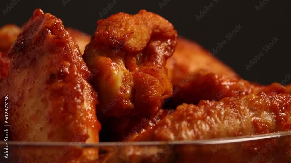 Cooked spicy buffalo wings smothered in hot sauce turning on table, close up shit