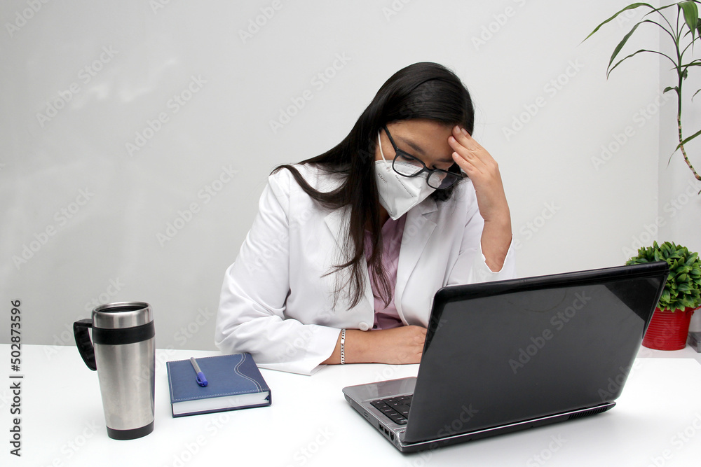 Latino medical doctor man with gown and face mask feeling sick with headache, migraine from burnout, exhaustion result of excessive and prolonged emotional, physical, and mental stress
