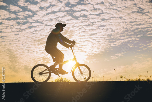 Silhouette of man relaxing, ride a bicycle along the bike lane in the park at the sunset.	