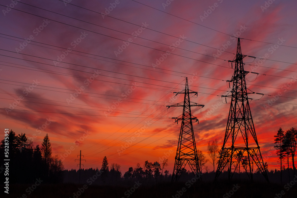 Electric pylons in the Estonian countryside in autumn during sunset. Dramatic sky in the background.