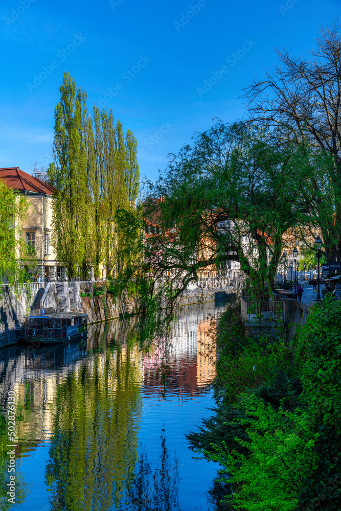Obraz premium Embankment of Ljubljanica river and old buildings in the historical center of Ljubljana, Slovenia at sunny spring day. Cityscape of the Slovenian capital Ljubljana over Ljubljanica river.