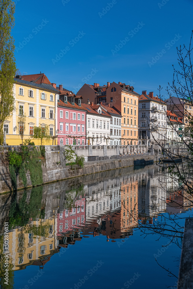 Embankment of Ljubljanica river and old buildings in the historical center of Ljubljana, Slovenia at sunny spring day. Cityscape of the Slovenian capital Ljubljana over Ljubljanica river.