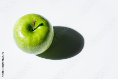 top view of shadow near green apple on white. photo