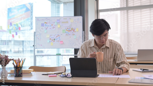 Handsome asian male manager holding coffee cup and working at modern office.