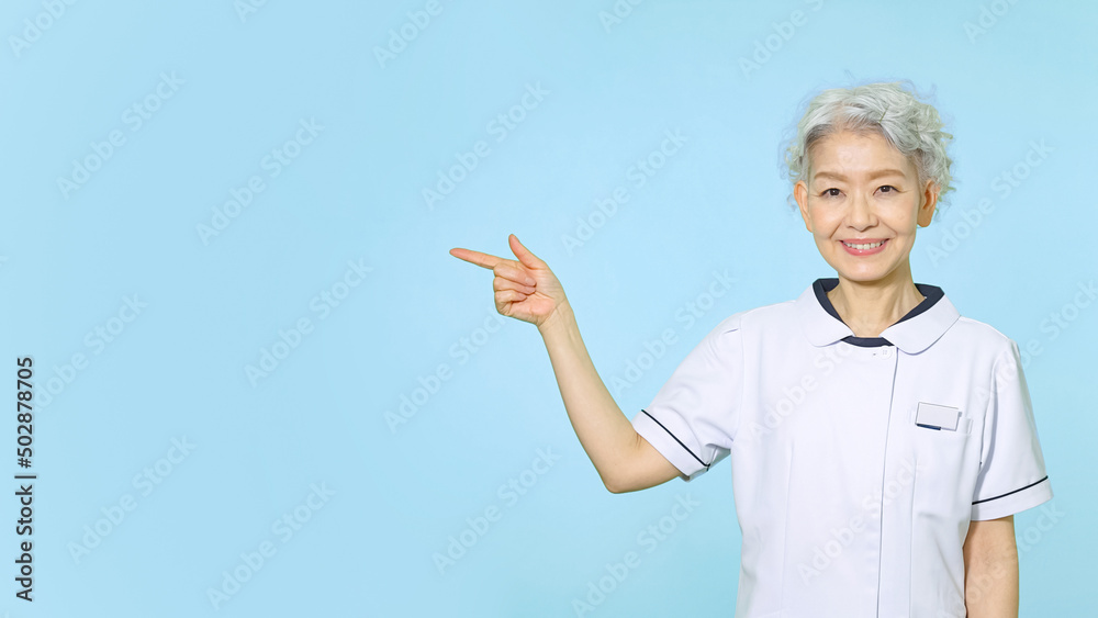 笑顔で指をさす白衣のシニア女性