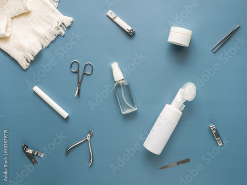 Top view of face and nail care set: towel, washing gel,nail file, nippers, scissors, tweezers, body oil, face and hand cream, tweezers, eyebrow oil. Spa and skin care concept. Blue background.Flat lay