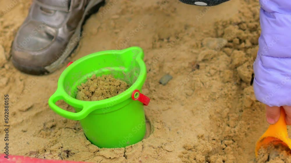 Close-up, a child digs sand, picks it up in a shovel and puts it in a bucket, children's games in the fresh air. Close-up, a child digs sand, picks it up in a shovel and puts it in a bucket, children's games in the fresh air.