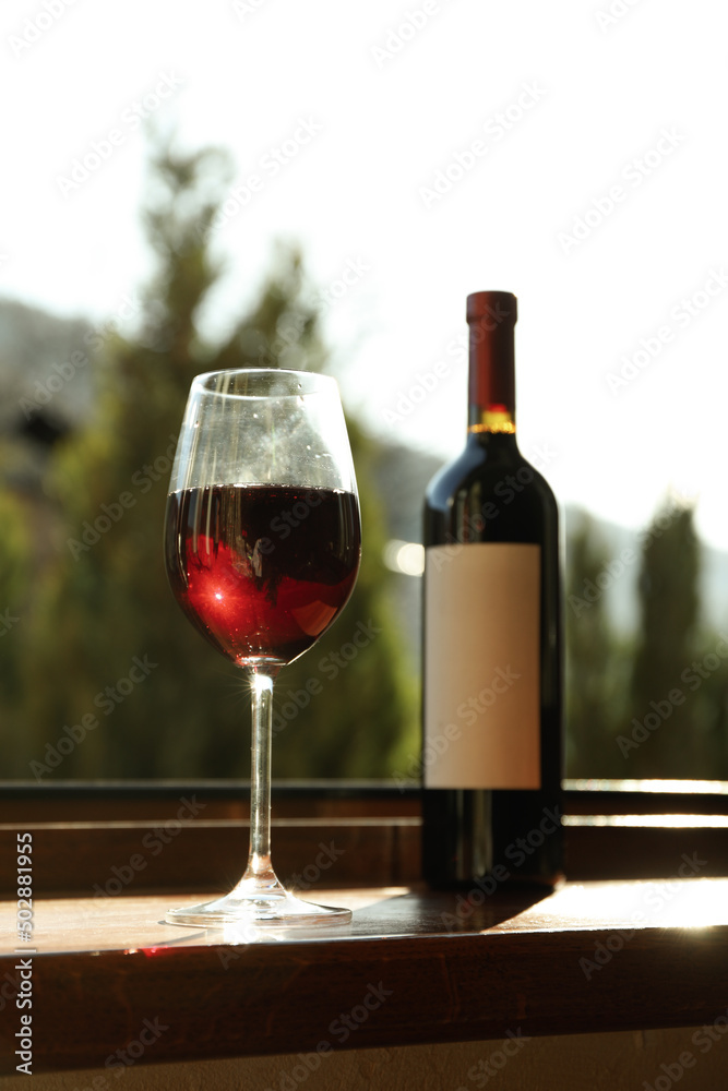 Glass and bottle of wine stands on wooden windowsill