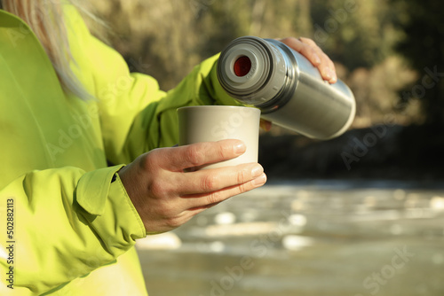 Woman pour drink from thermos to cup outdoor