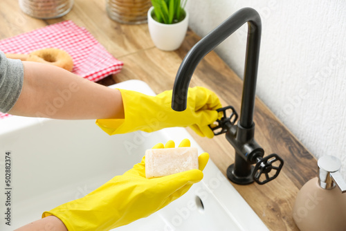 Woman in rubber gloves wetting soap in sink, closeup