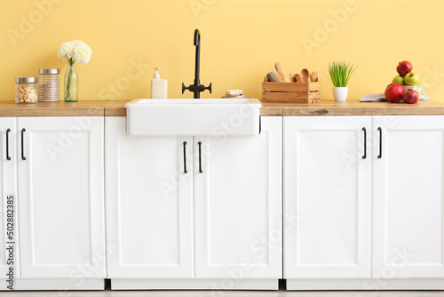Counter with kitchen utensils and modern sink near color wall