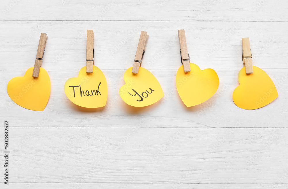 Heart shaped sticky notes with text THANK YOU and clothespins on white wooden background Heart shaped sticky notes with text THANK YOU and clothespins on white wooden background