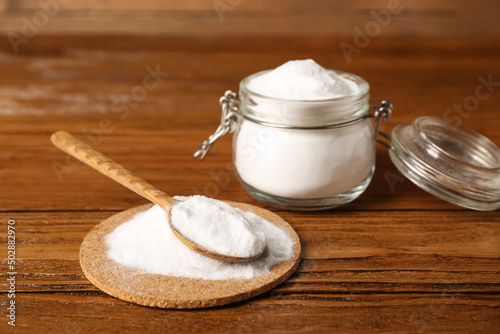 Pile of baking soda and spoon on wooden background