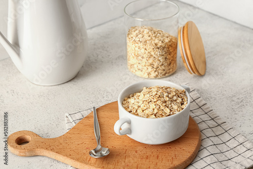 Wooden board with bowl of raw oatmeal on light background