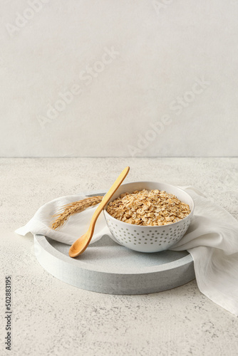 Bowl of raw oatmeal and spoon on light background