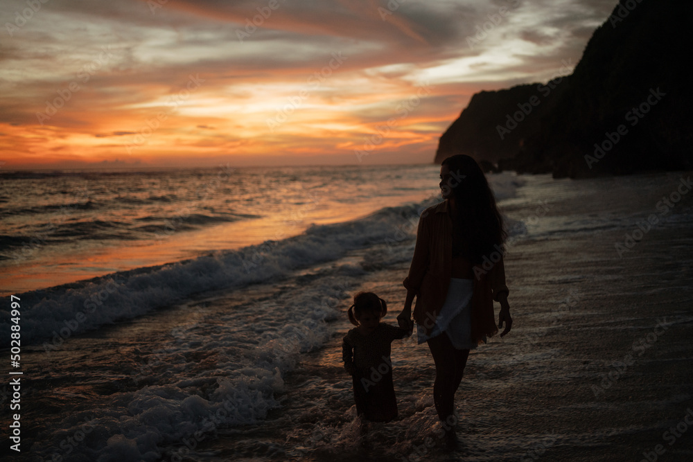 Young woman with her little cute girl walk  on beach during sunset. Cheerful .caucasian  daughter walking and playing with mother on beach, silhoutte