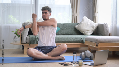 Handsome man warming up, stretching arms before workout at home.