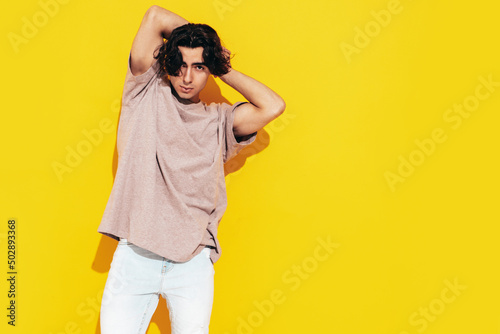 Portrait of handsome confident stylish hipster lambersexual model.Man dressed in over size T-shirt and jeans. Fashion male isolated in studio. Posing near yellow wall