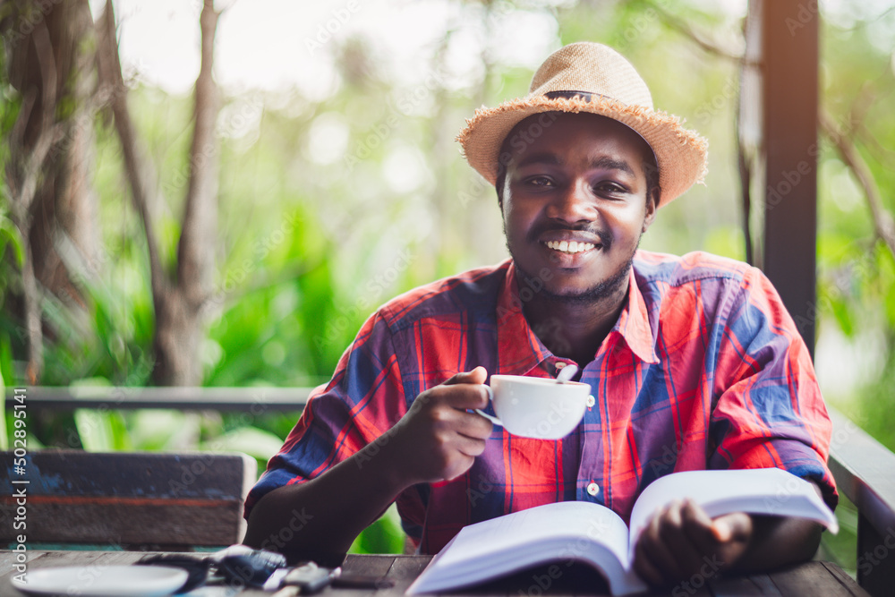 African traveler in a hat with a book and a cup of coffee thinking and looking camera African traveler in a hat with a book and a cup of coffee thinking and looking camera