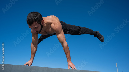 Shirtless man doing a handstand on a parapet by the sea. 