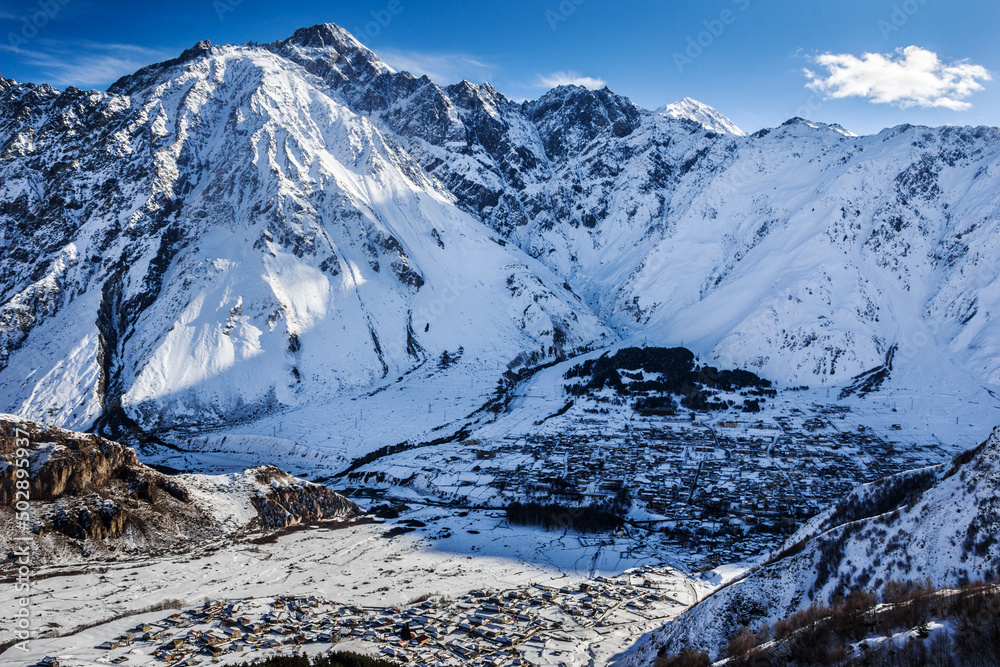Obraz premium Mountain landscape with the Georgian ancient village of Kazbegi Stepantsminda located in the lowland is located in the Caucasus Mountains, near Mount Kazbek, near the Russian-Georgian border