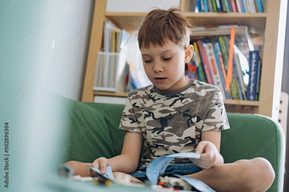 Little caucasian boy constructing a car with plastick blocks reading instructions book