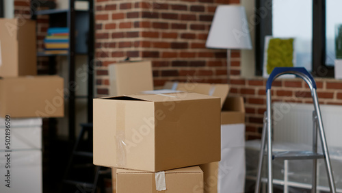 Stacks of cardboard boxes in empty real estate property with furniture, lamp and interior decor. Nobody in living room apartment with carton storage containers and cargo packages. Close up. © DC Studio