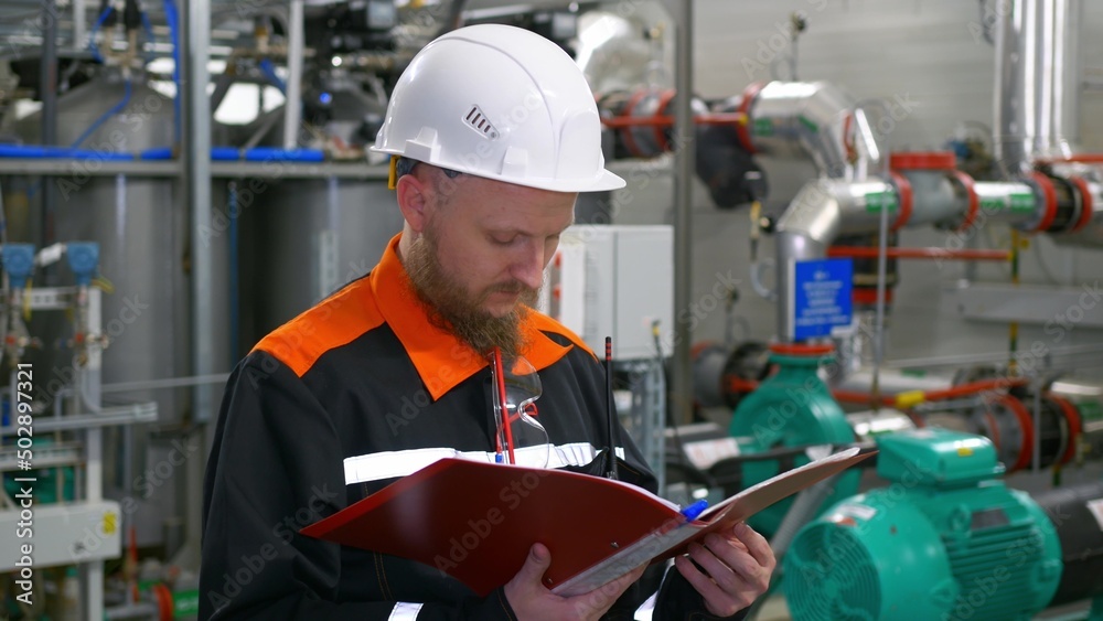 An industrial engineer in a white helmet conducts an inspection at his workplace, uses a folder with records, checks the availability of equipment and its parameters in work the petrochemical industry An industrial engineer in a white helmet conducts an inspection at his workplace, uses a folder with records, checks the availability of equipment and its parameters in work the petrochemical industry