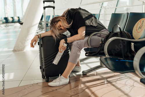 Fotografie, Obraz Tired and sleepy blond woman in casual clothes with luggage, leaning on bags, sitting in airport terminal