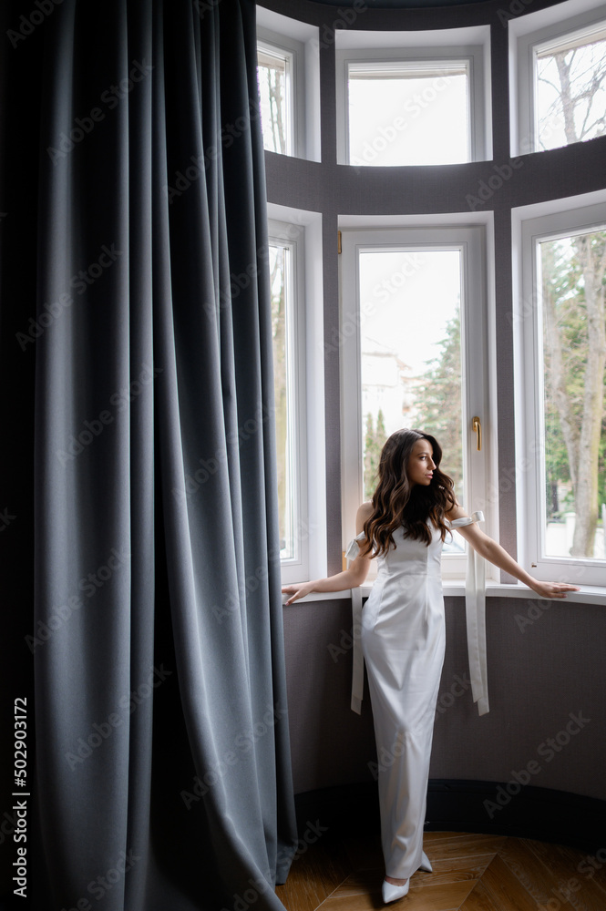 Beautiful young bride posing on the background of a window with a wedding bouquet