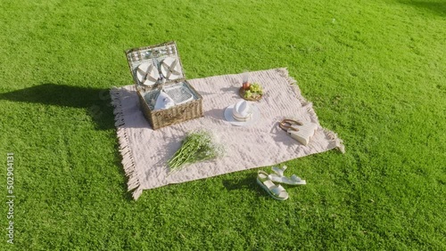 Aerial 4K slow motion commercial footage picnic on green grass. Basket with apples and plates on bright green lawn. Still life on green grass, food for a picnic at summer sunset. Video series 2 of 6 photo