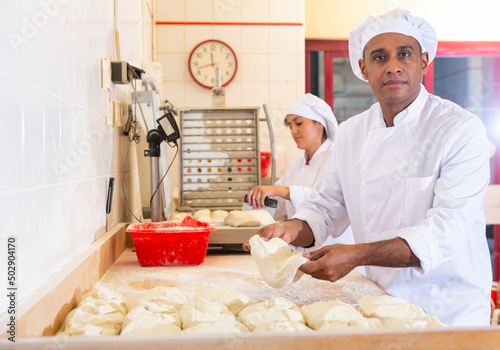 Latin american man working with his wife in family bakery, forming bread loaves from raw dough