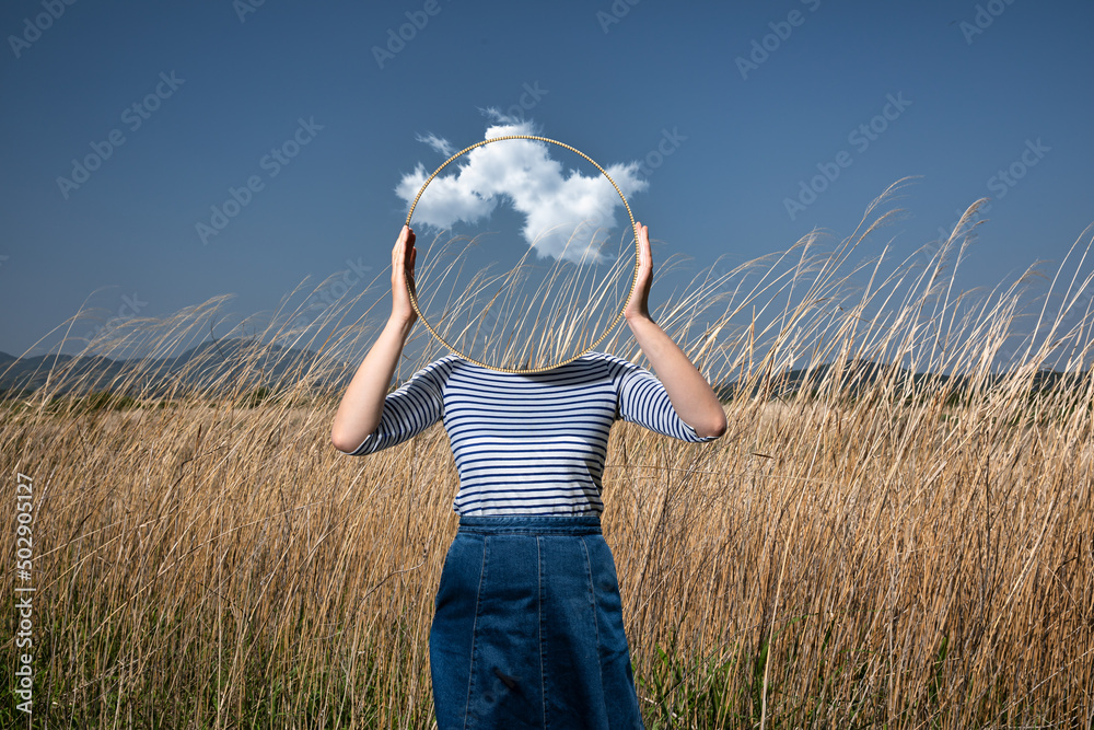 Surrealism with a woman holding a mirror and covering her face in the field with a transparent background behind the mirror - obrazy, fototapety, plakaty 