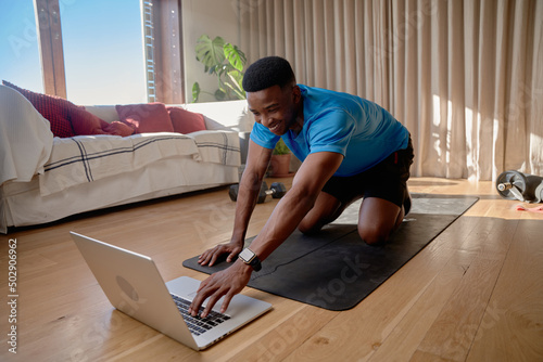 Young African american male working out at home doing an online class using laptop