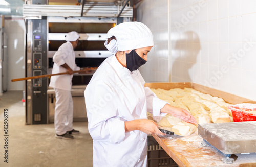 Bakery worker cuts raw dough with a knife
