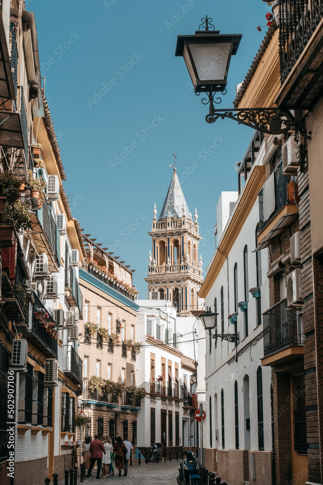 Sunny street in Triana district in Seville, in background bell tower of church