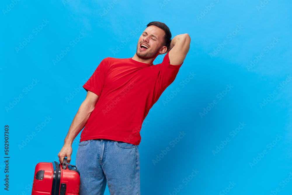 Overjoyed excited happy tanned handsome man in red t-shirt preparing for holiday hold big suitcase posing isolated on blue studio background. Copy space Banner Mockup. Trip journeys concept Overjoyed excited happy tanned handsome man in red t-shirt preparing for holiday hold big suitcase posing isolated on blue studio background. Copy space Banner Mockup. Trip journeys concept