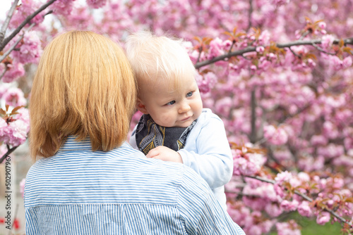 young mother with little son in her hands in park with Sakura Cherry blossom tree. Happy mother and child.