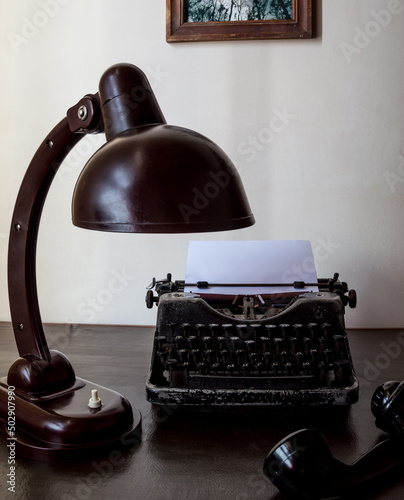 Vintage typewriter, desk lamp and old phone handset on the table.